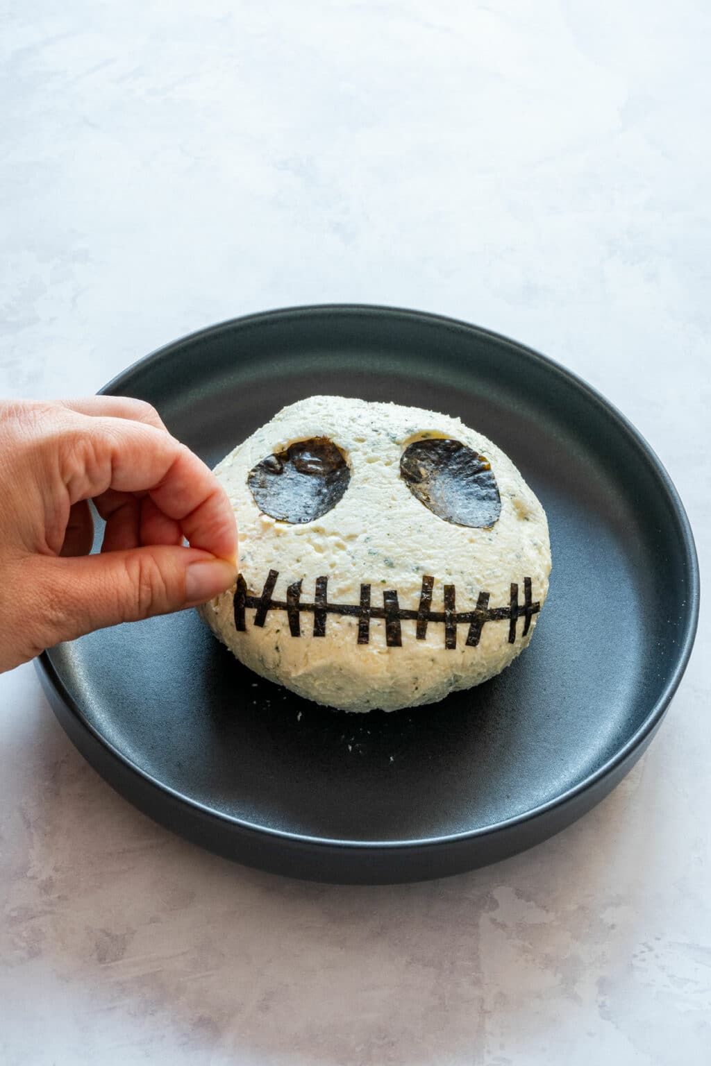 Adding nori strips to form the stitched smile on the cheese ball.