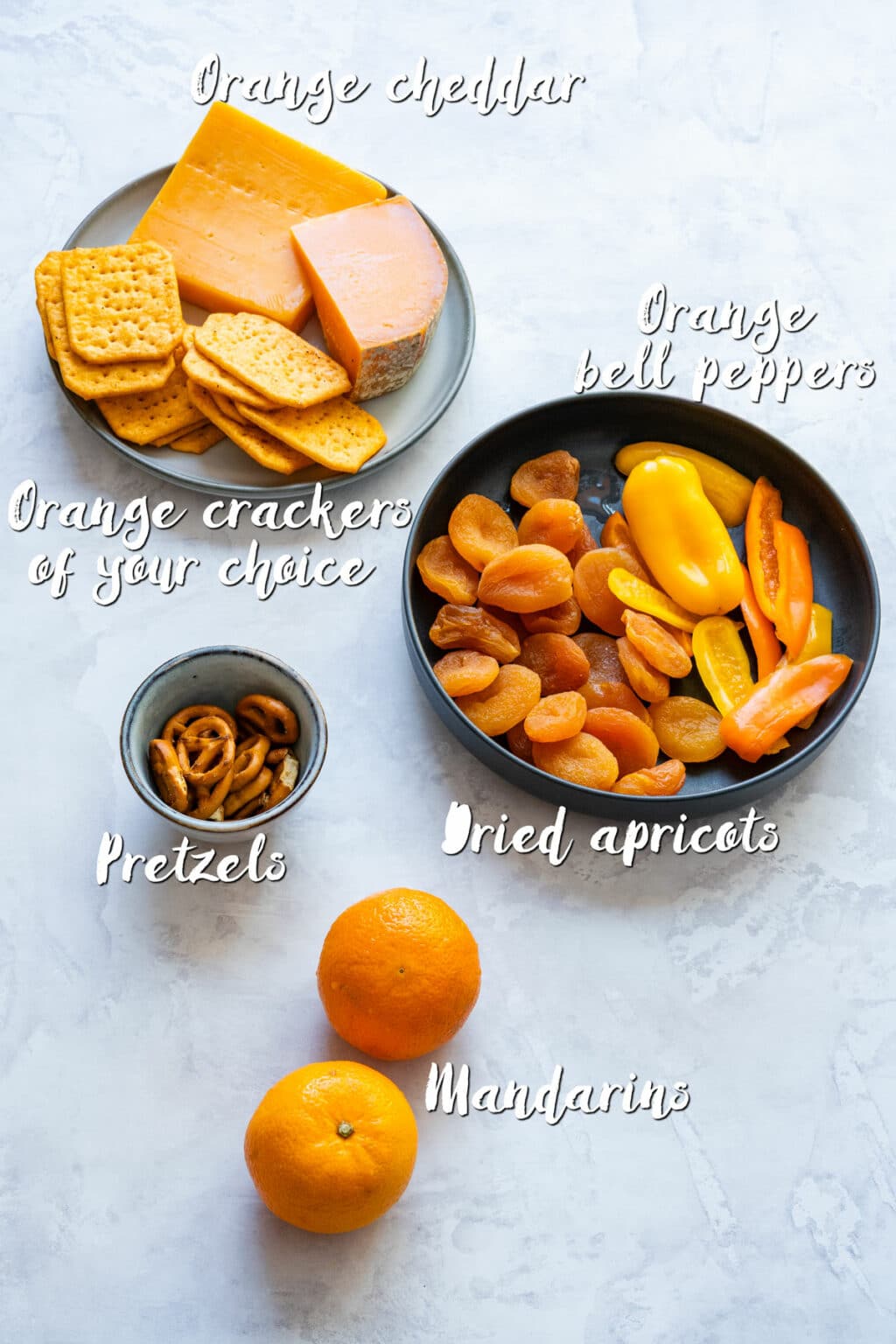 Ingredients for an orange fall board: cheddar, crackers, dried apricots, mandarins, mini peppers, pretzels.