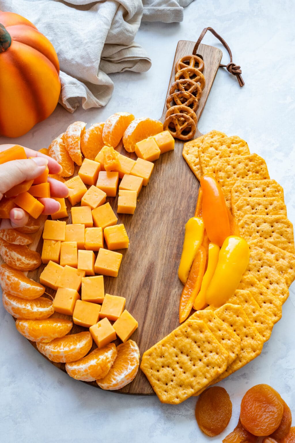 Arranging cheddar cubes between mandarin segments and peppers to form the pumpkin shape.
