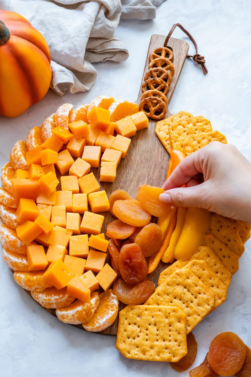 Adding dried apricots beside the cheddar on the pumpkin snack board.