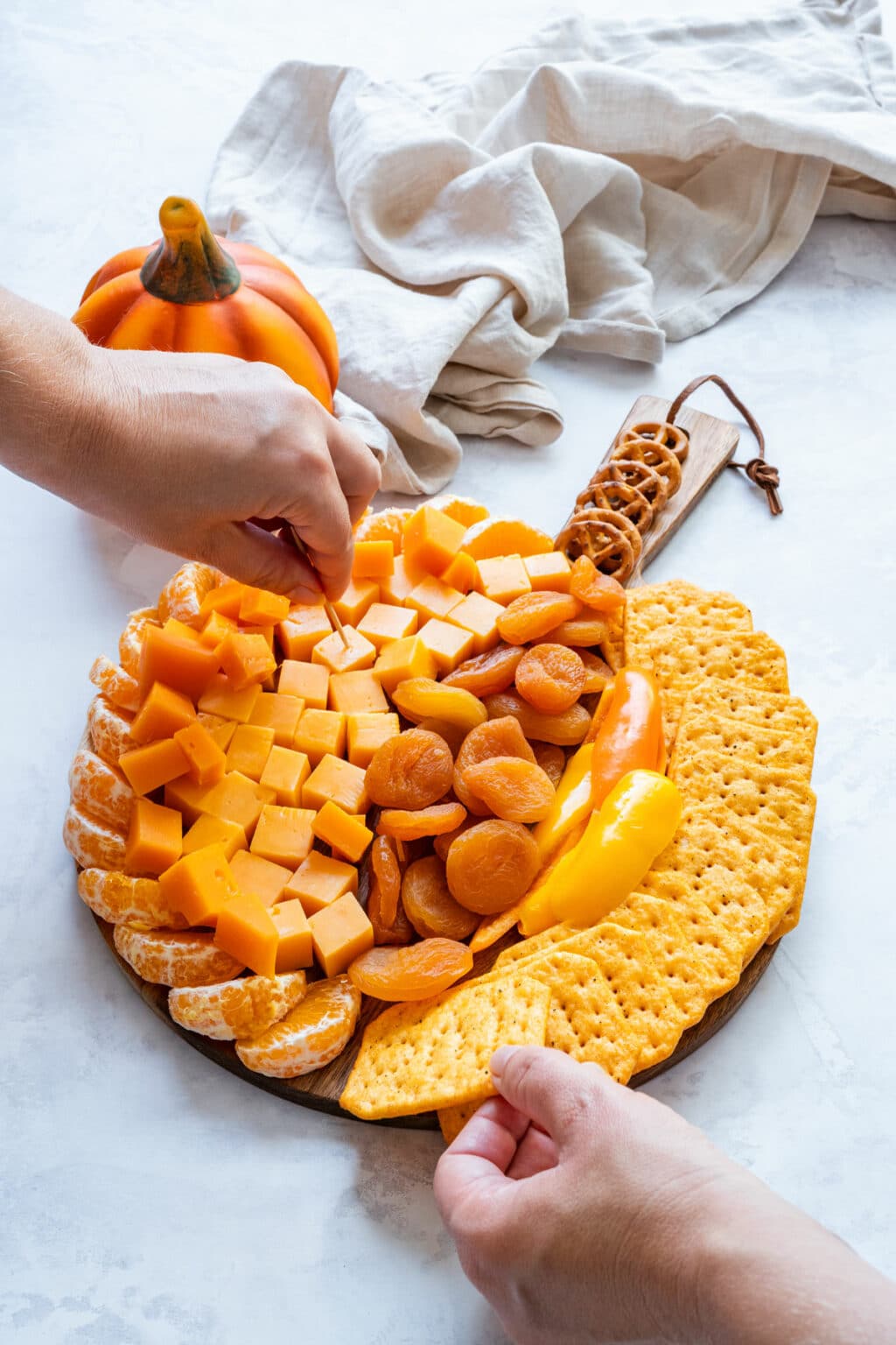 Hands tucking crackers around the edge and adjusting toppings on the board.