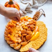 Hands tucking crackers around the edge and adjusting toppings on the board.