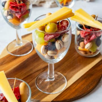 Charcuterie cups in clear glasses with salami, grapes, olives, nuts, blueberries and cheese sticks