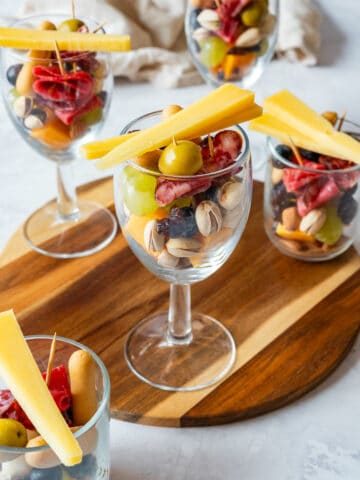 Charcuterie cups in clear glasses with salami, grapes, olives, nuts, blueberries and cheese sticks