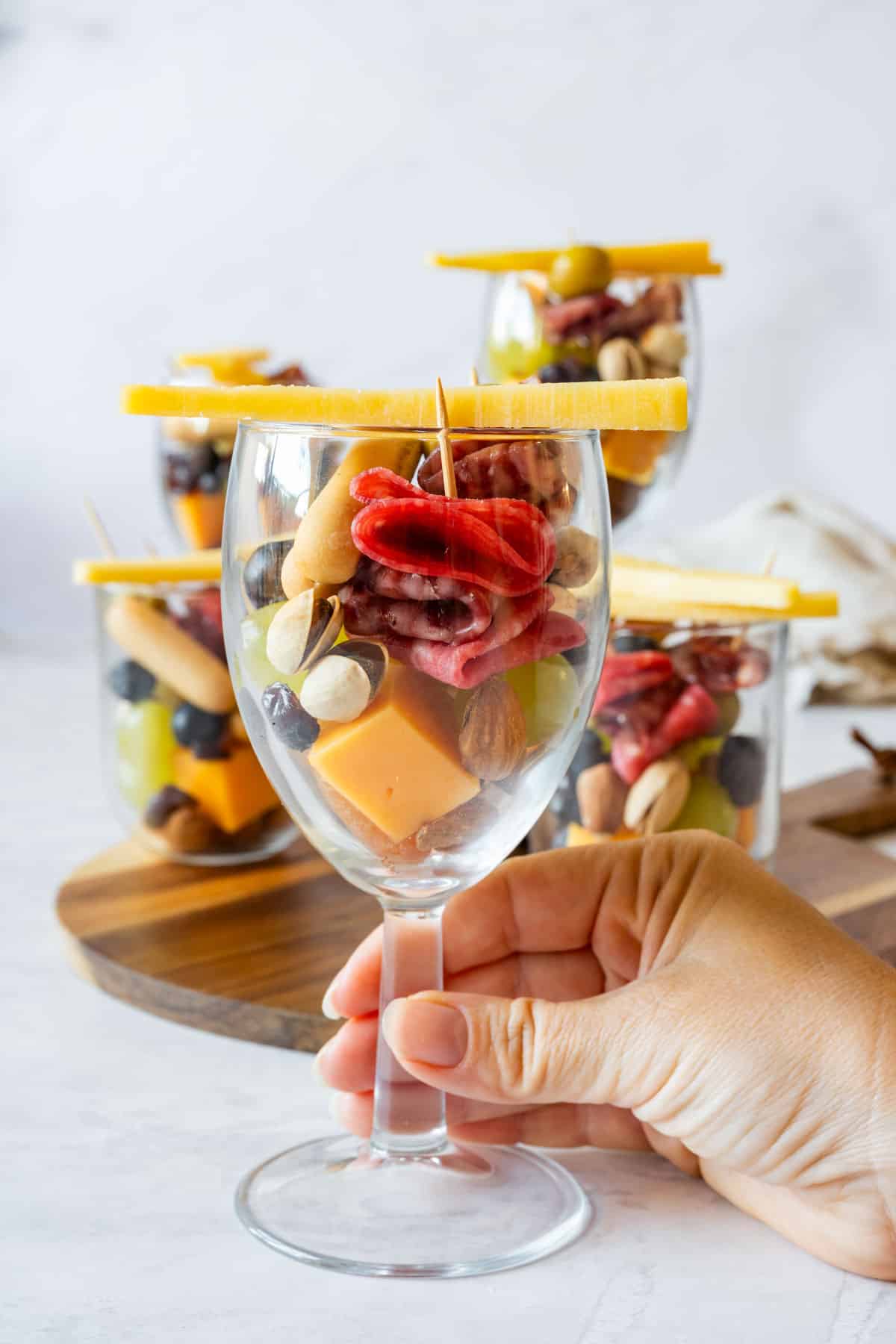 Hand holding a filled individual charcuterie cup appetizer with salami, cheddar, grapes, nuts and blueberries.