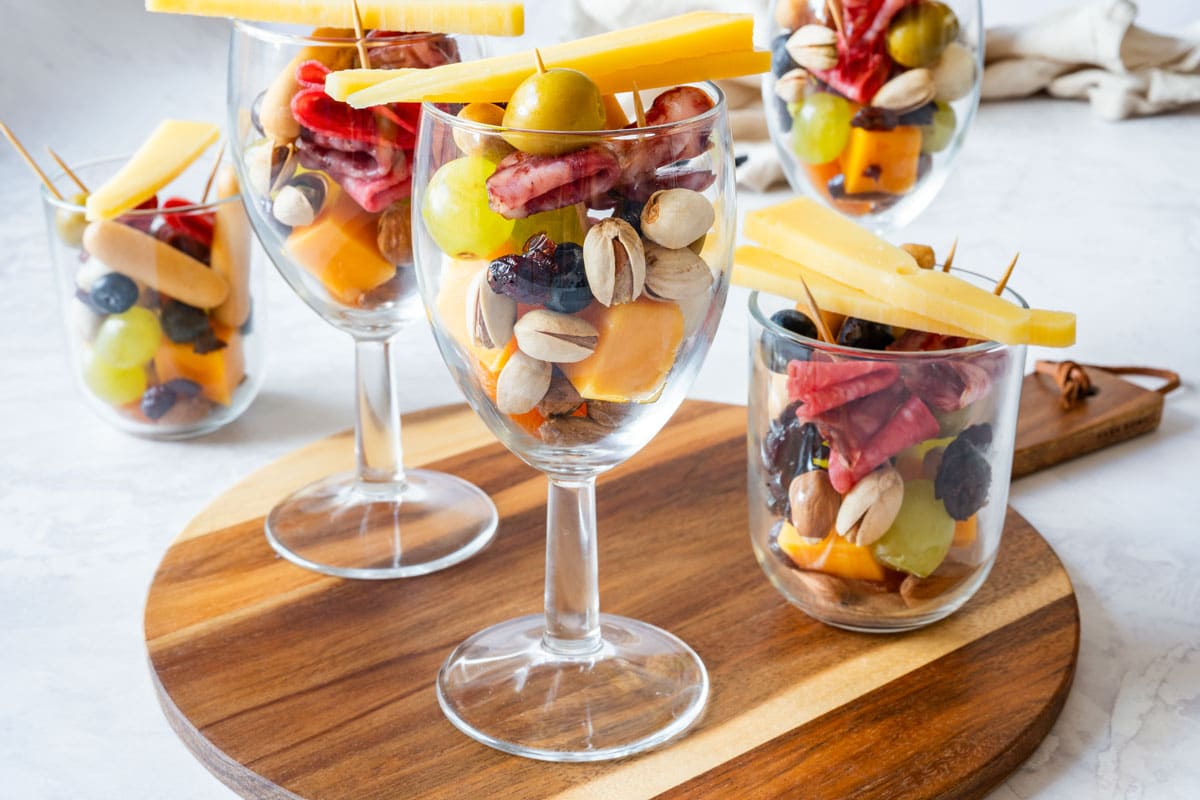 Party snack cups on a serving board, topped with cheese sticks and toothpick skewers.