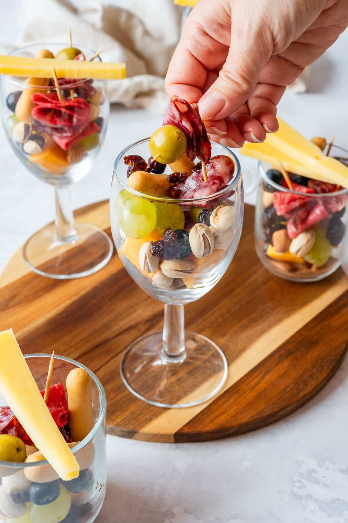 Guest grabbing a toothpick skewer with olive and cured meat from an individual snack cup.