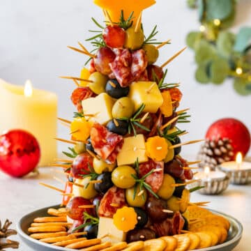 Small Christmas charcuterie tree made with cheese, olives, grapes and salami on a plate surrounded by crackers.