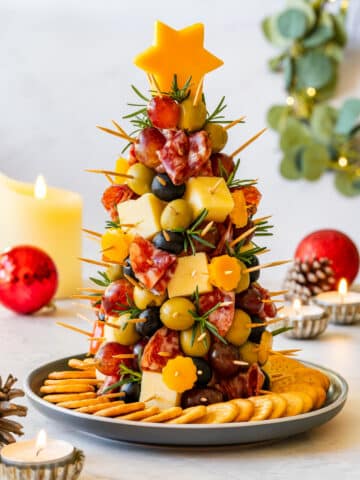 Small Christmas charcuterie tree made with cheese, olives, grapes and salami on a plate surrounded by crackers.