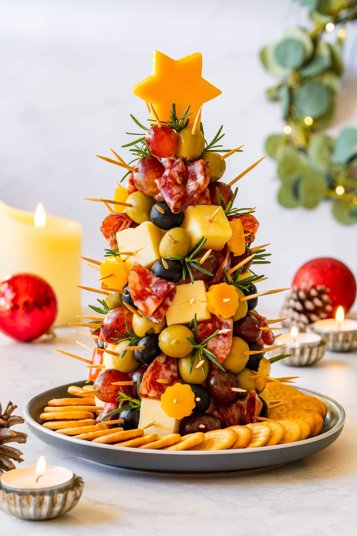 Small Christmas charcuterie tree made with cheese, olives, grapes and salami on a plate surrounded by crackers.