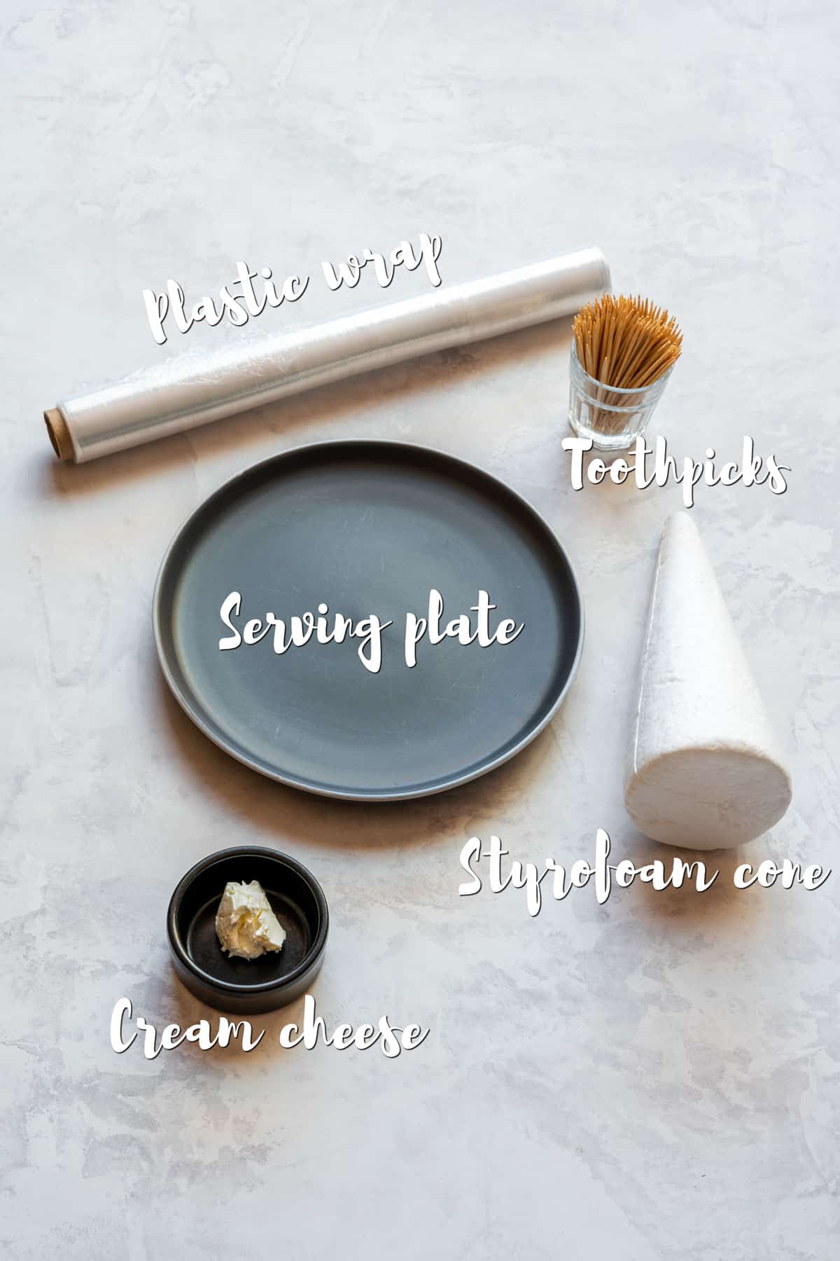 Serving plate, foam cone, toothpicks, cream cheese and plastic wrap laid out as tools for making a charcuterie tree.