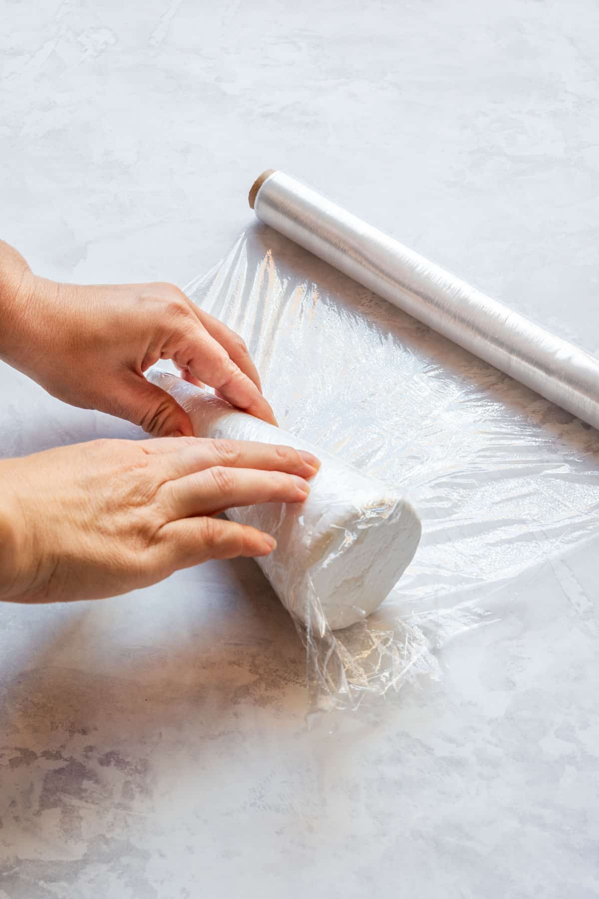 Hands wrapping a foam cone tightly in plastic wrap to prepare the base for the charcuterie tree.