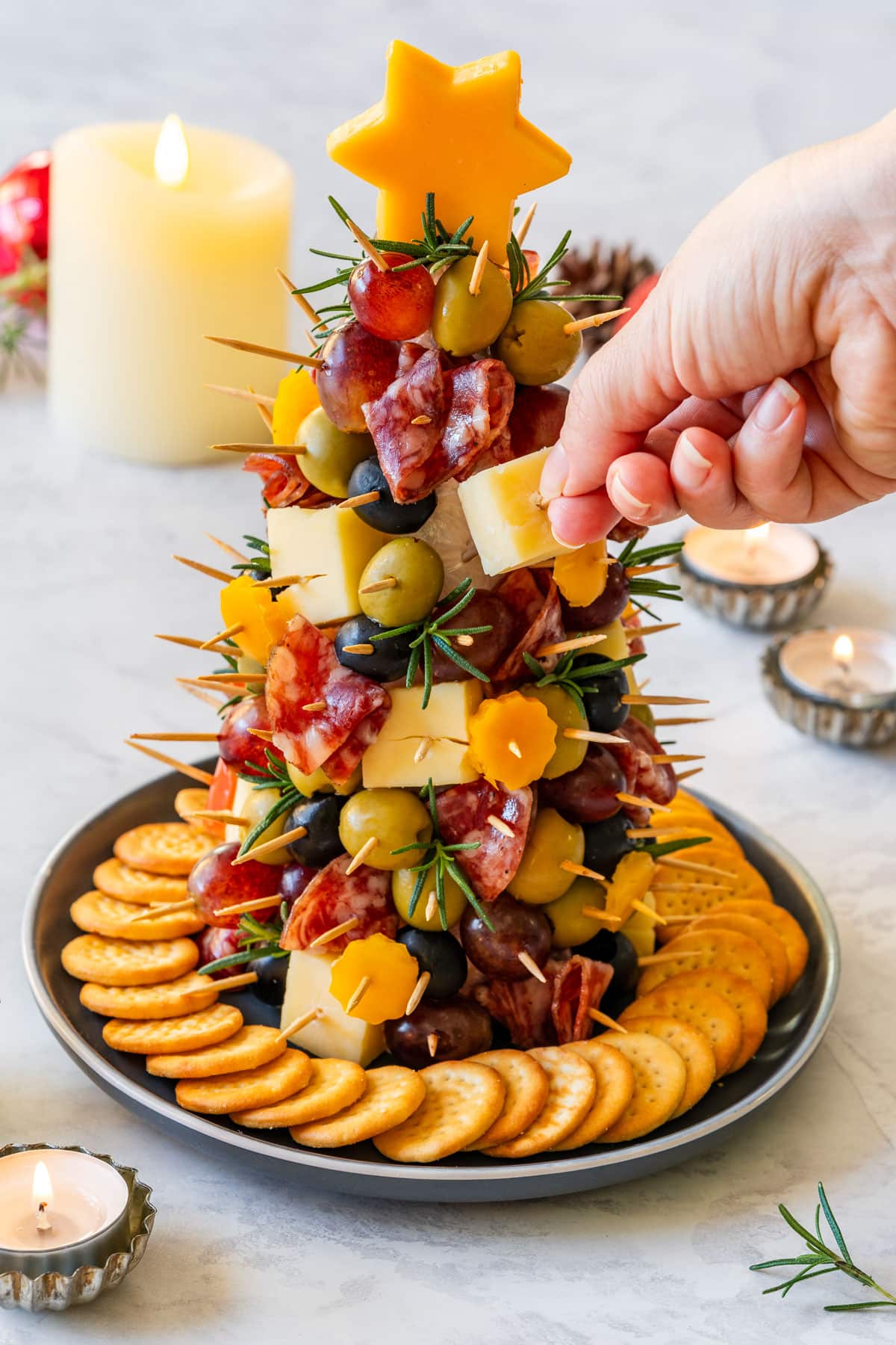 Hand taking a cheese cube from the finished charcuterie tree served on a plate with crackers.