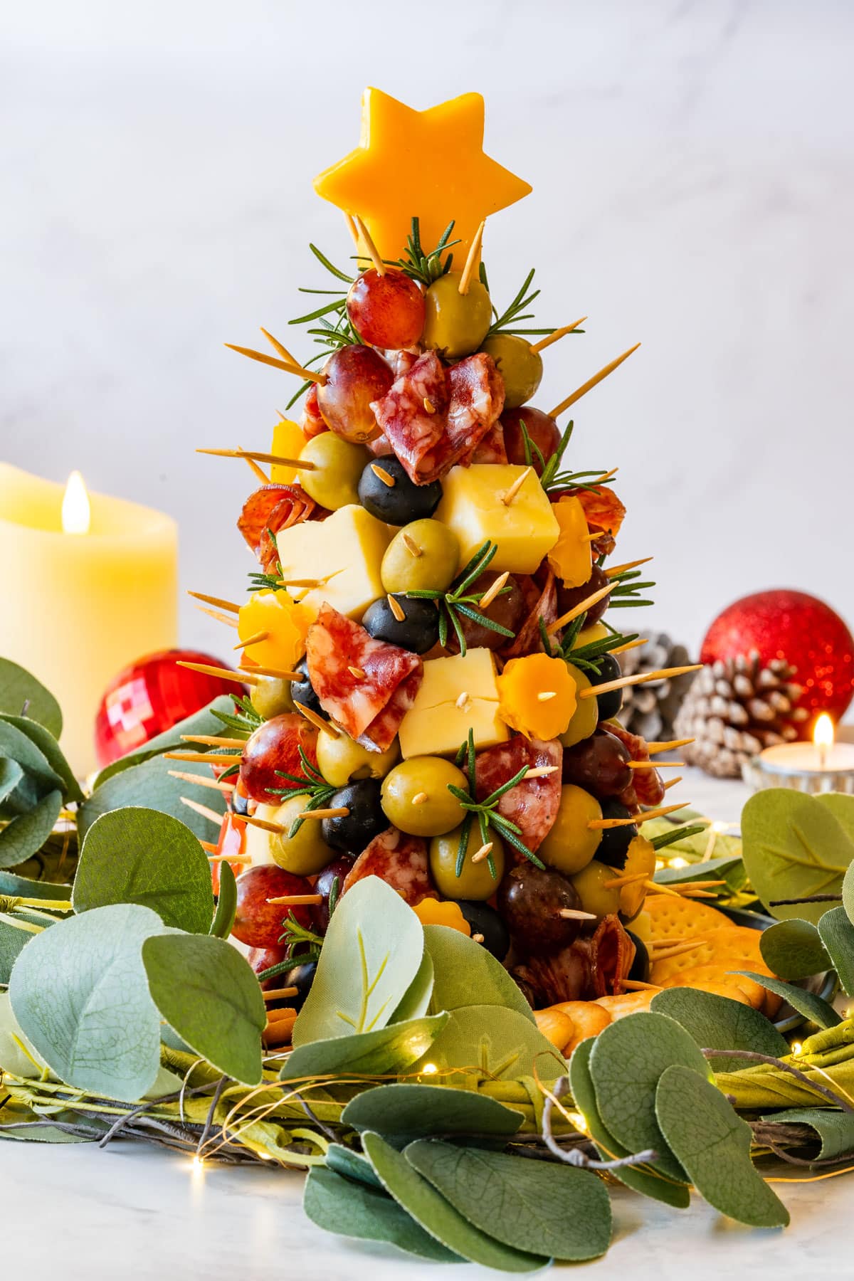 Christmas charcuterie tree centerpiece topped with a cheese star and rosemary, styled with greenery, lights and candles.