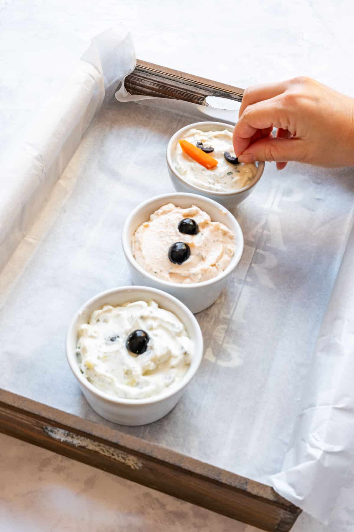Placing olive eyes and a carrot nose on the top dip bowl to make the snowman face for the Christmas veggie tray.