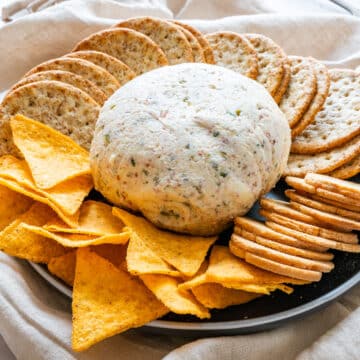 Bacon and olive cheese ball on a platter with tortilla chips and assorted crackers.
