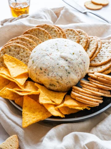 Bacon and olive cheese ball on a platter with tortilla chips and assorted crackers.