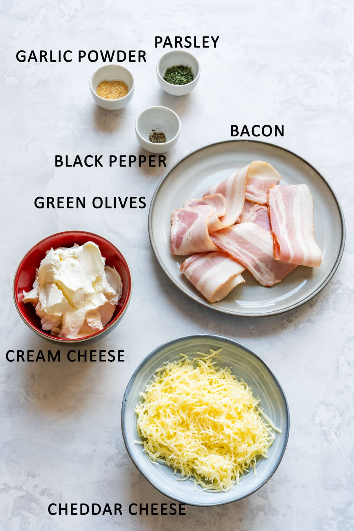 Ingredients for bacon and olive cheese ball labeled on a light surface.