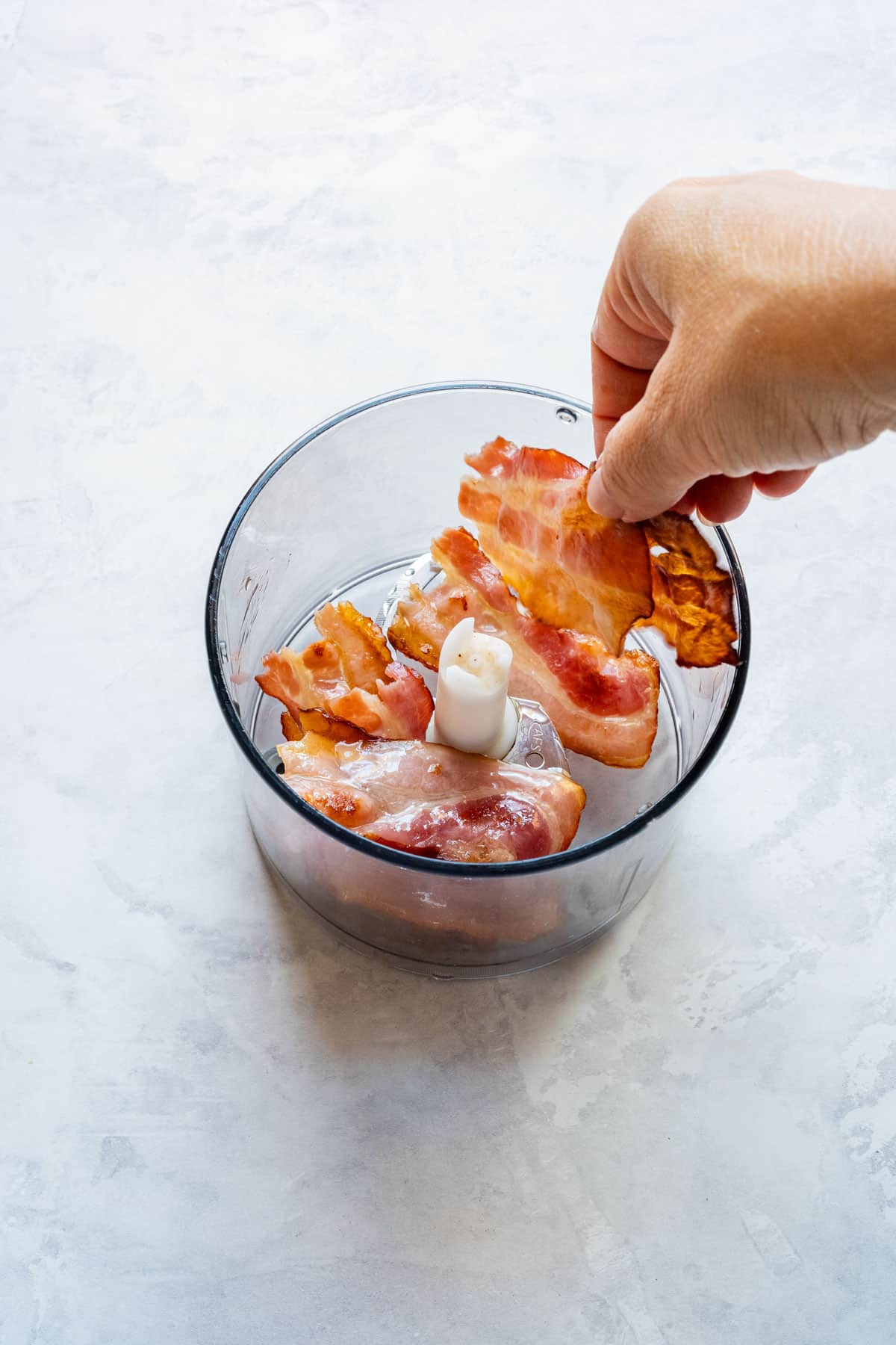 Adding cooked bacon strips to a small food processor.