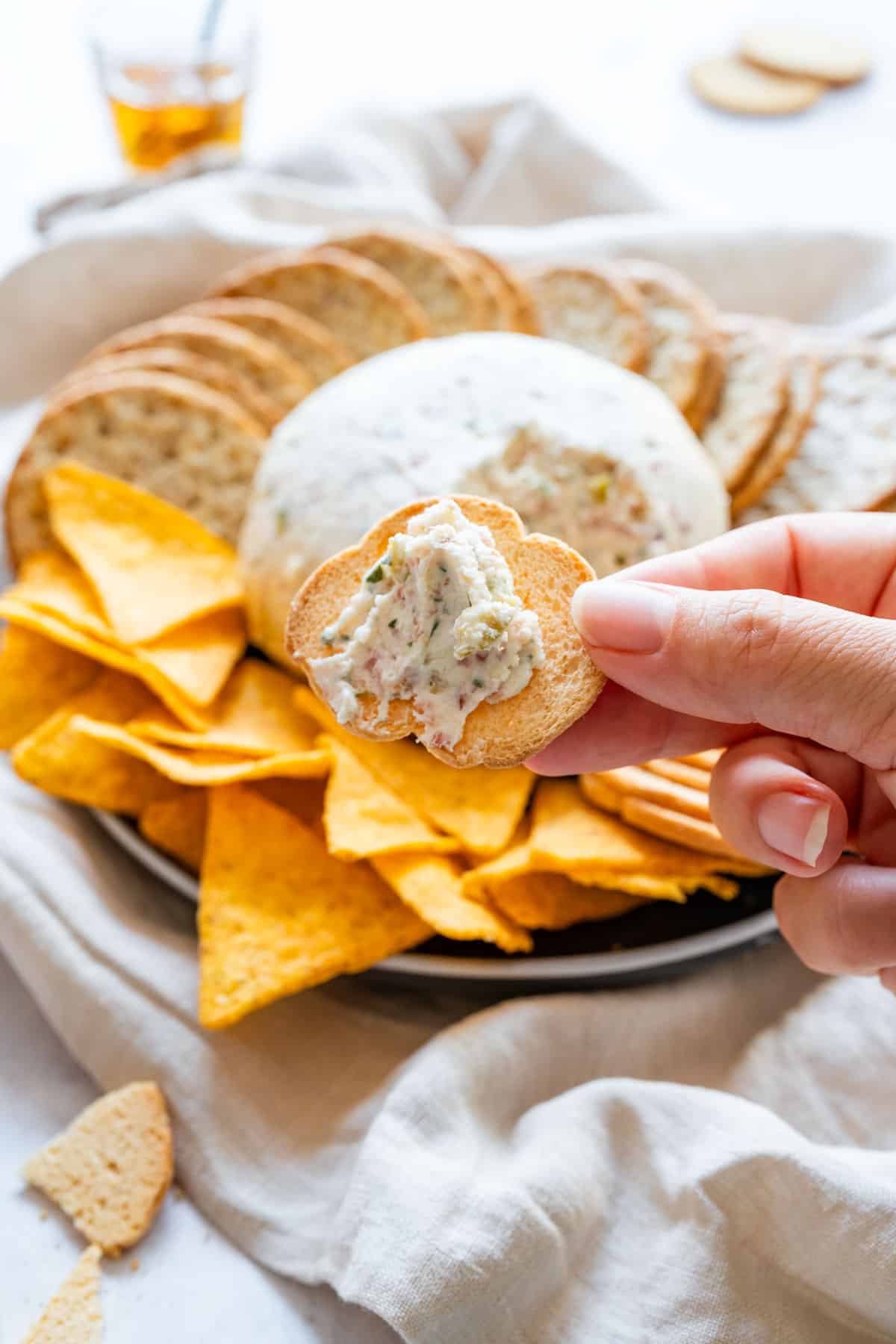 Hand holding a crostini topped with bacon and olive cheese ball spread.