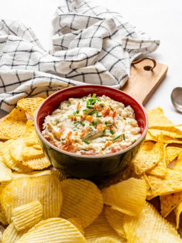Loaded baked potato dip served with ruffled potato chips and tortilla chips on a wooden board.