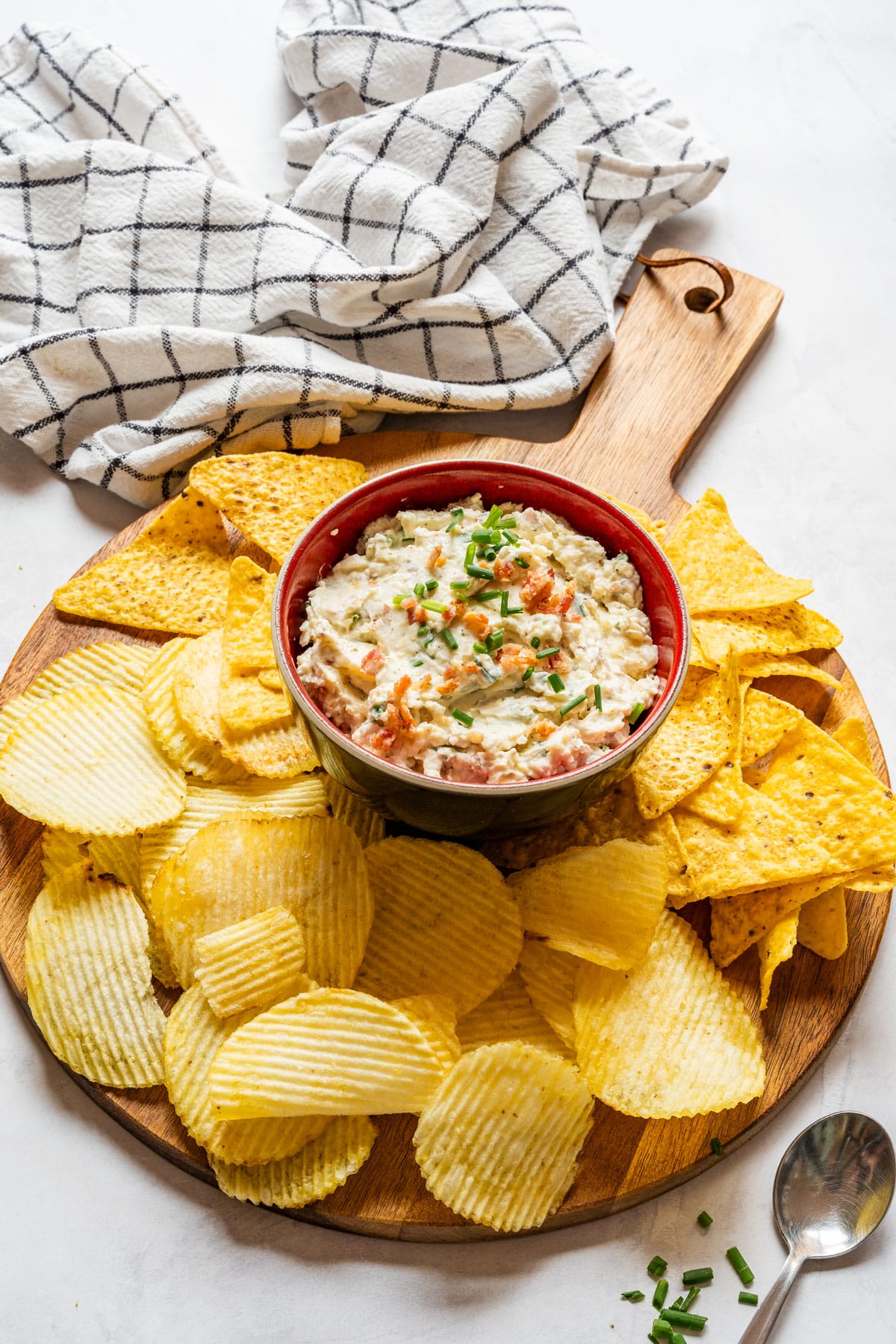 Loaded baked potato dip in a bowl surrounded by potato chips and tortilla chips.