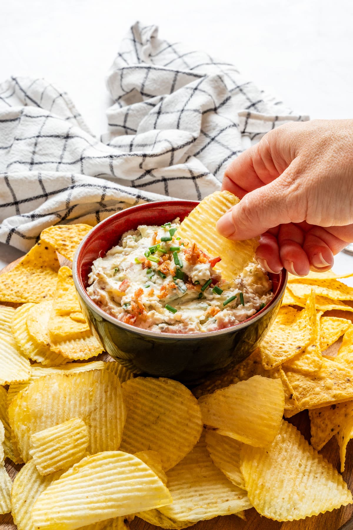 Hand dipping a ruffled potato chip into bacon and cheddar dip.