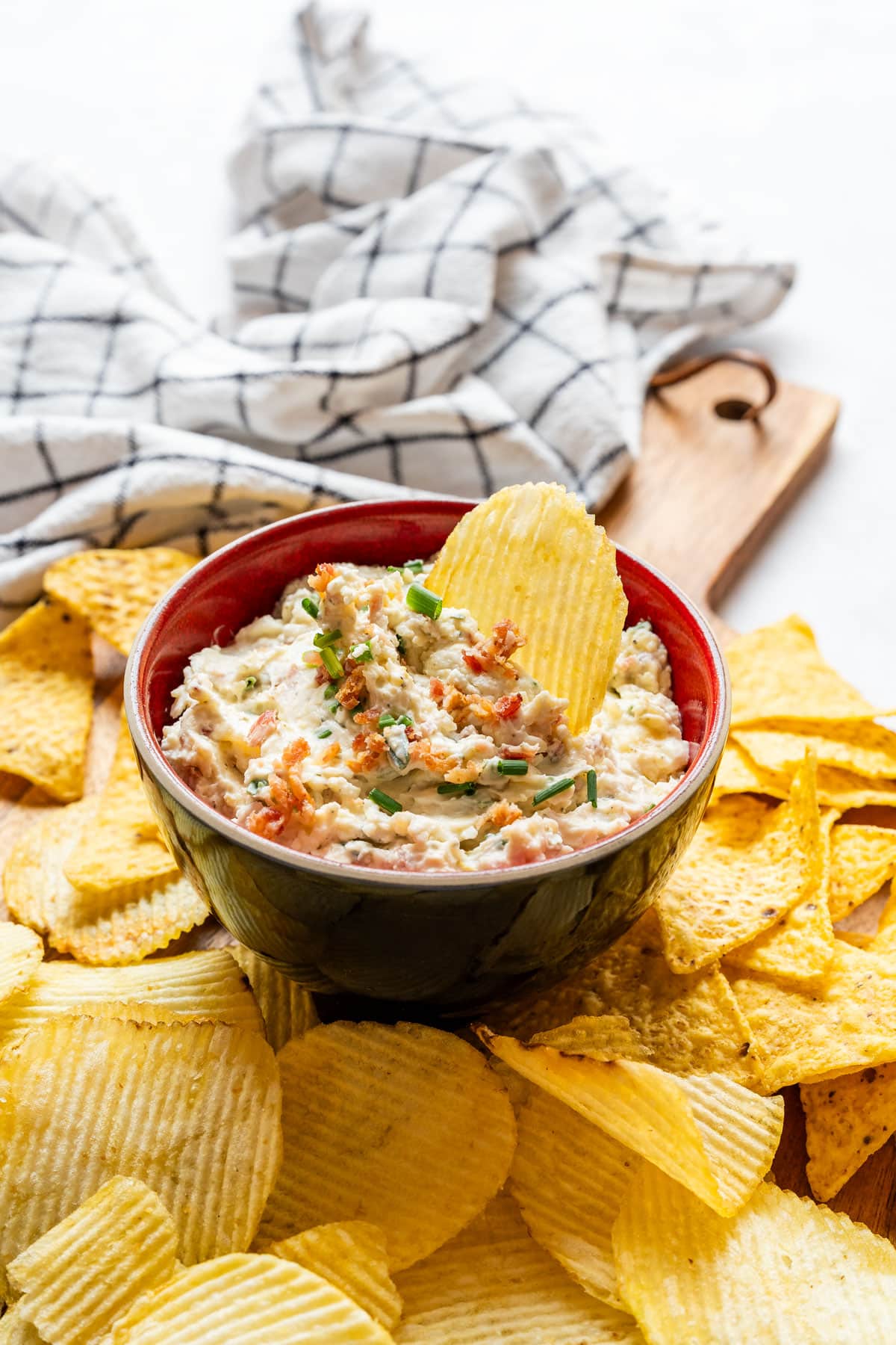 Close-up of bacon cheddar dip topped with chives and a potato chip.