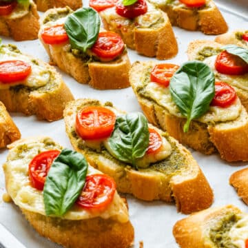 Baked pesto crostini with cheese, cherry tomatoes and fresh basil on a baking sheet.