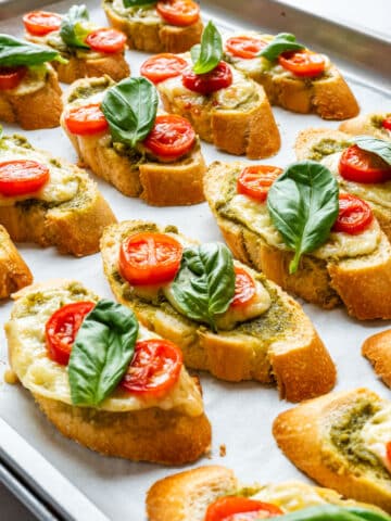 Baked pesto crostini with cheese, cherry tomatoes and fresh basil on a baking sheet.