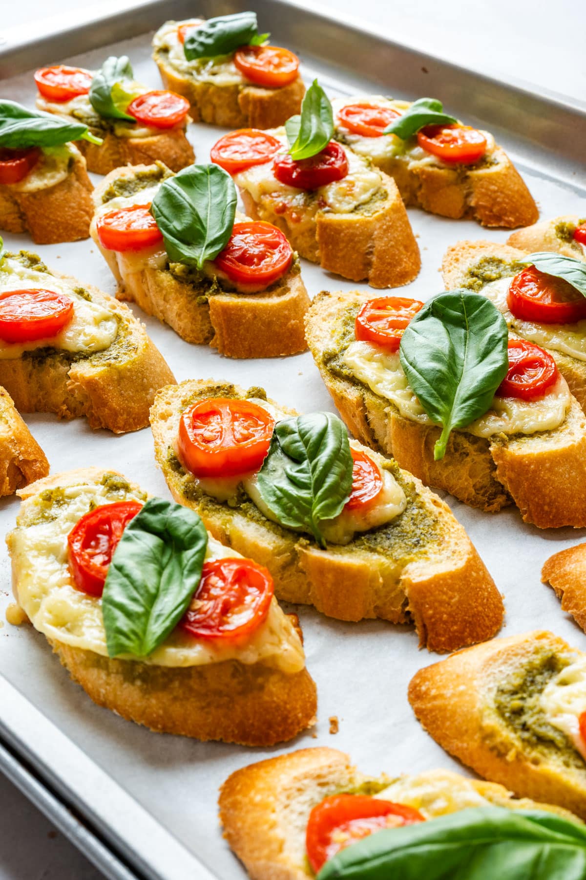 Baked pesto crostini with cheese, cherry tomatoes and fresh basil on a baking sheet.