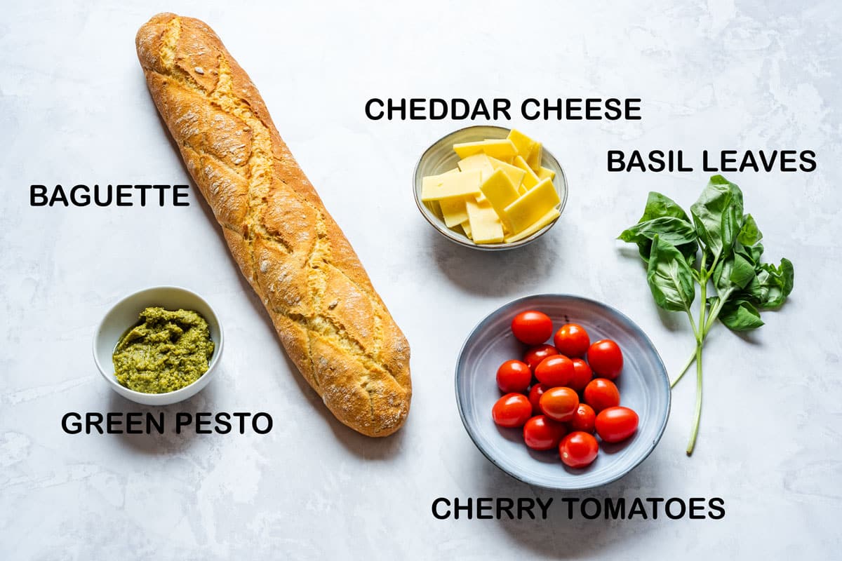 Ingredients for this crostini recipe: baguette, green pesto, cheddar cheese, cherry tomatoes and basil.