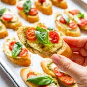 Hand holding a baked crostini with melted cheese, cherry tomatoes and fresh basil.