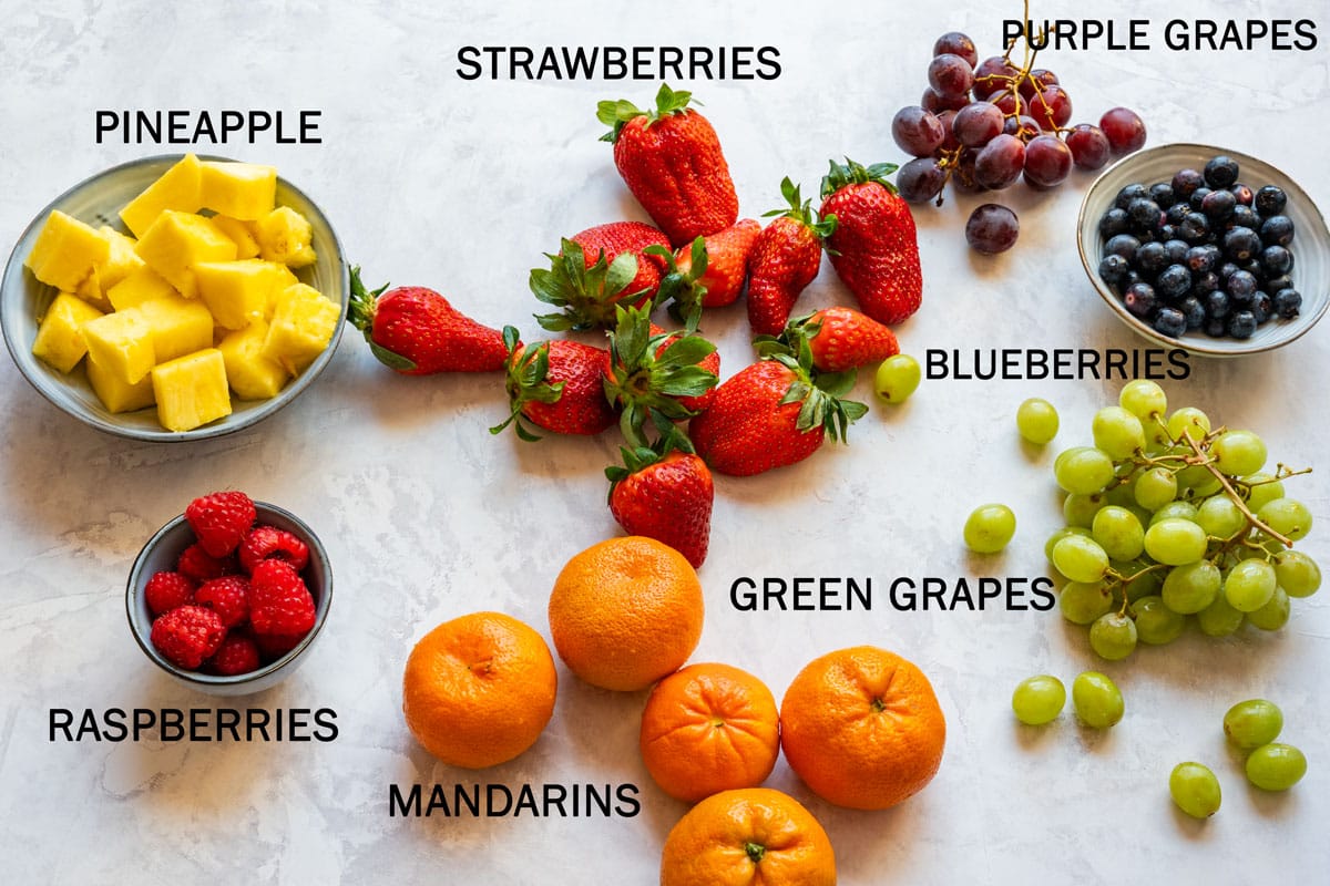 Fruit platter ingredients with strawberries, raspberries, mandarins, pineapple, blueberries, green grapes and purple grapes.