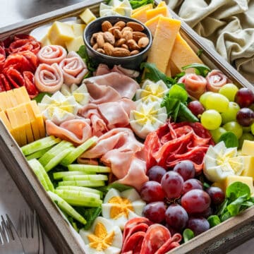 Spring charcuterie board with salami, ham, cheese, cucumber, grapes, almonds and hard-boiled eggs cut like flowers.