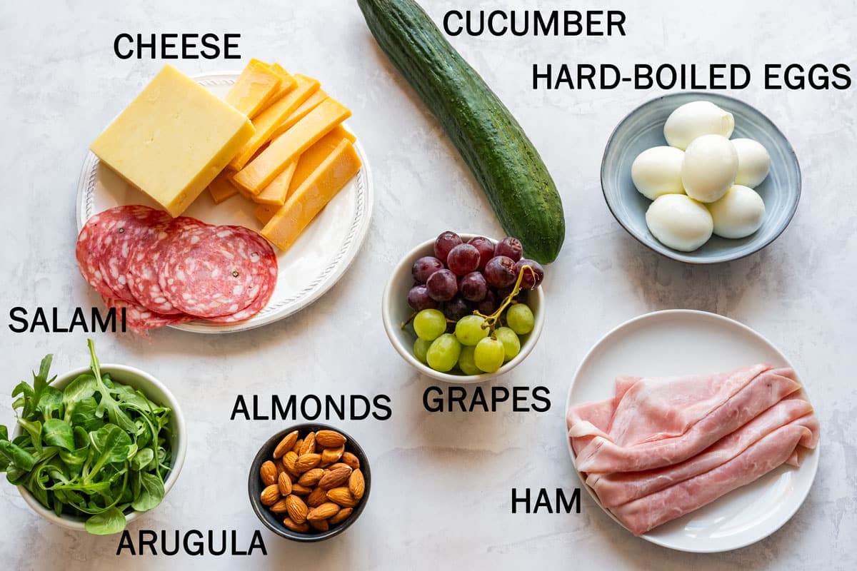 Ingredients for the board with cheese, salami, ham, cucumber, grapes, arugula, almonds and hard-boiled eggs.