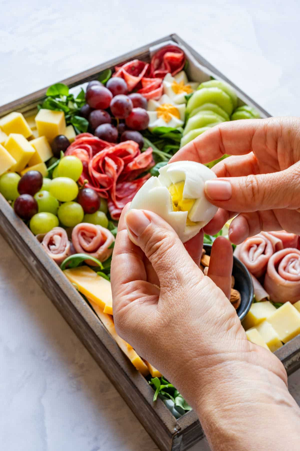 Hands holding a hard-boiled egg cut into a flower shape over the assembled board.