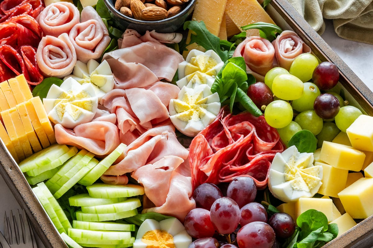 Close-up of the board with salami roses, grapes, cucumber, cheese and egg flowers.
