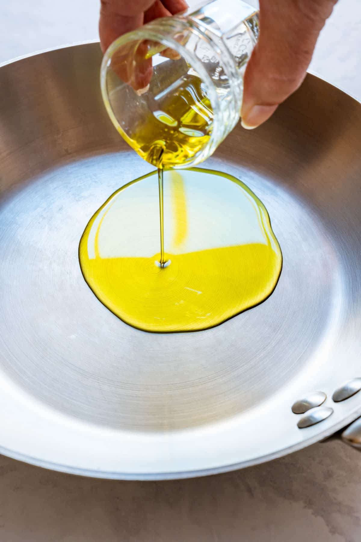 Olive oil being poured into a stainless steel skillet.