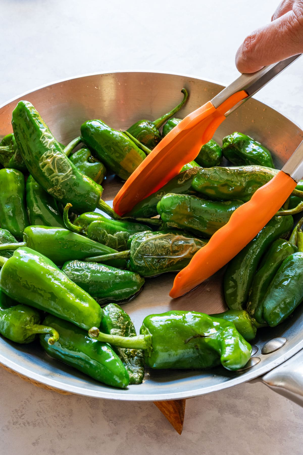 Padrón peppers in a skillet being turned with orange tongs.