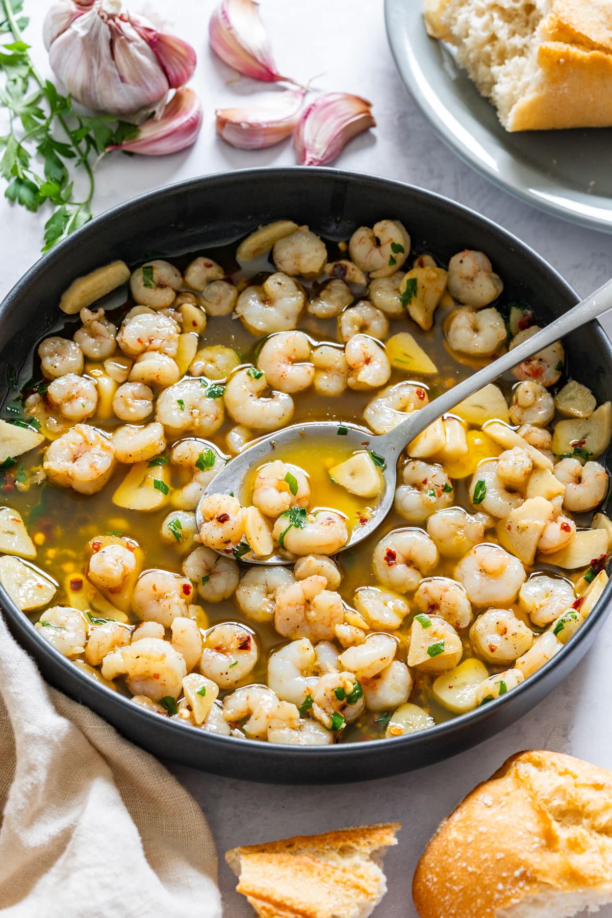 Small shrimp cooked in garlic and olive oil, lifted on a spoon over a black pan.