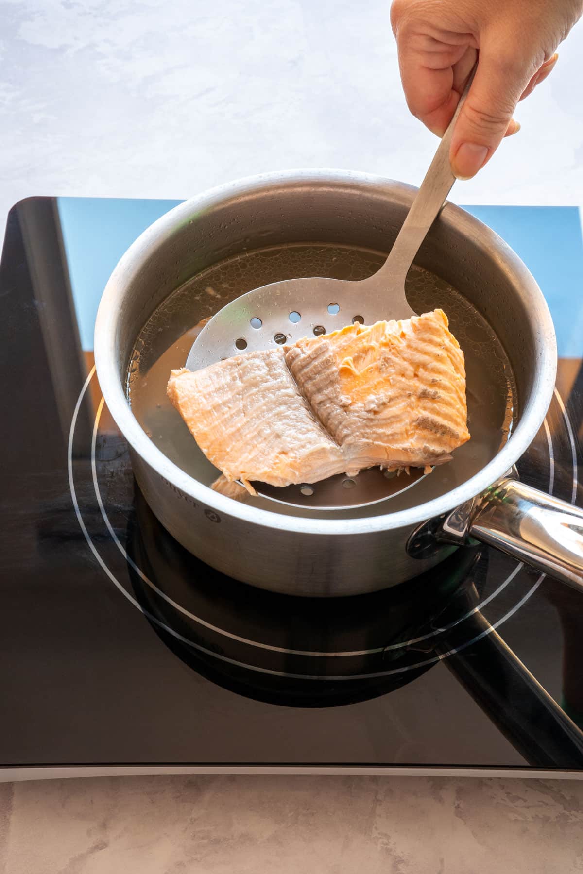 Cooked salmon fillet being lifted from the pot with a slotted spoon.