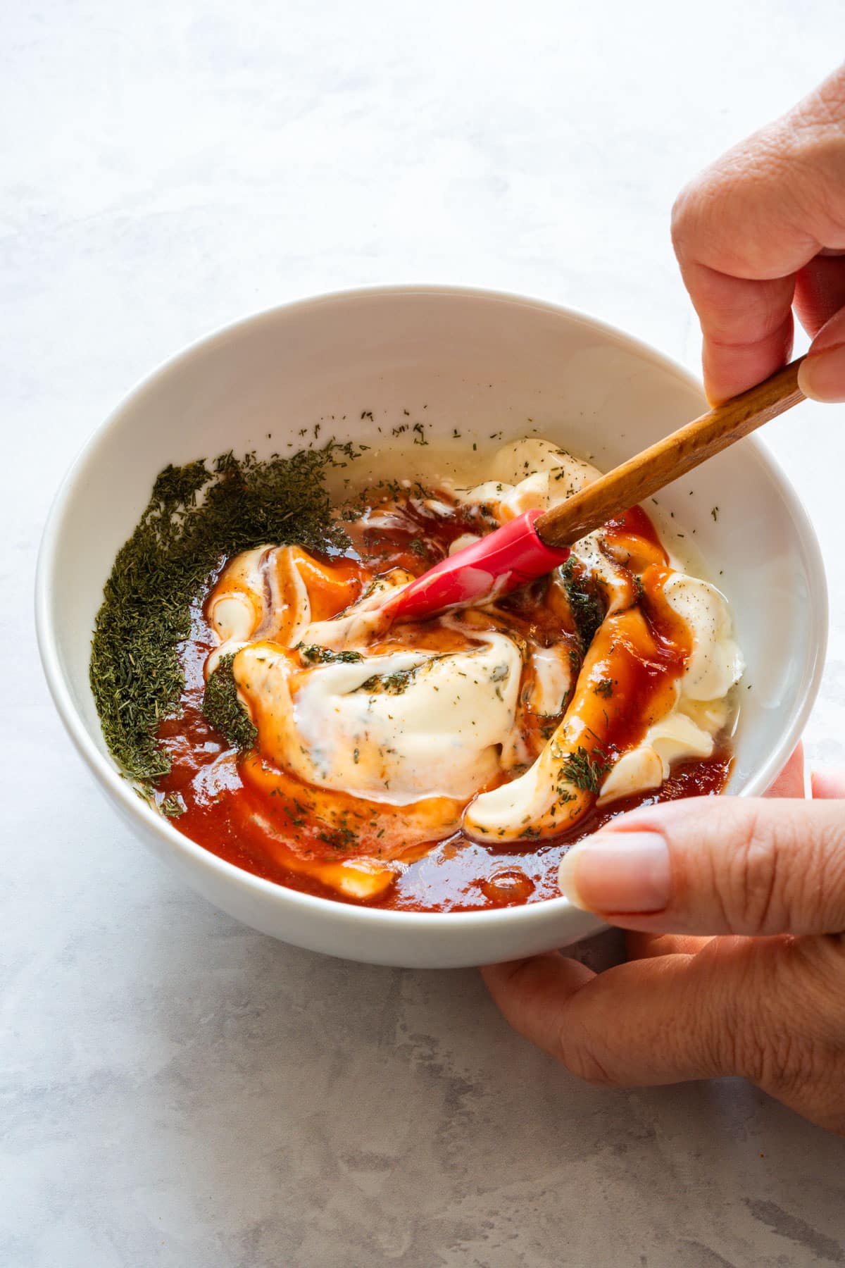 Mayonnaise, ketchup and dried dill being mixed in a small bowl.