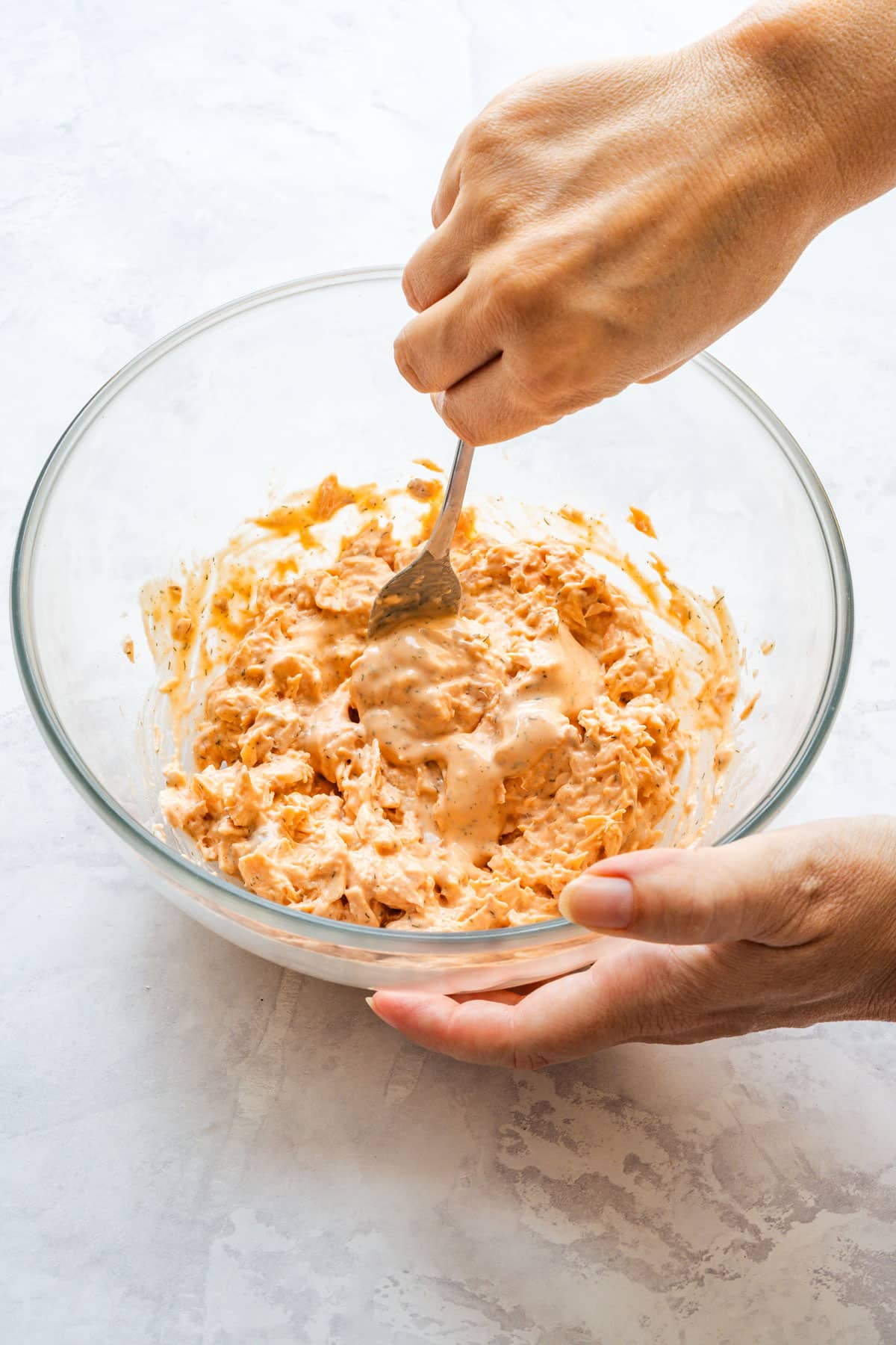 Creamy sauce being mixed into flaked salmon in a glass bowl.