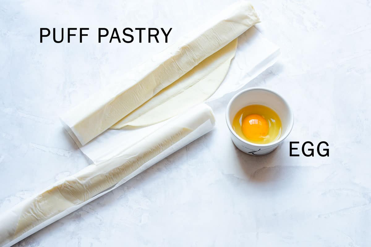 Two sheets of puff pastry and an egg in a small white bowl.