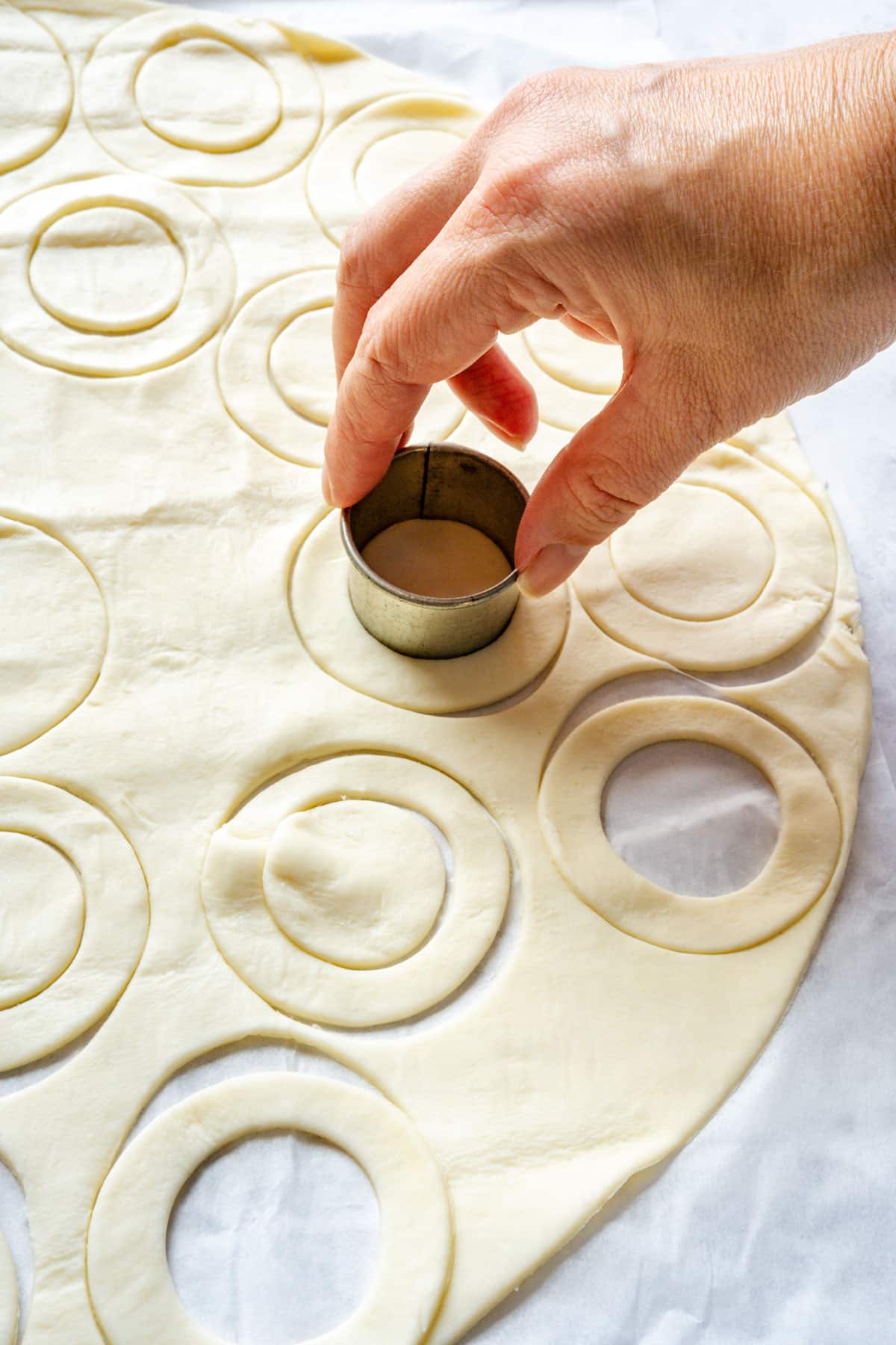 A small round cutter cutting the center from a larger puff pastry circle, with pastry rings around it.