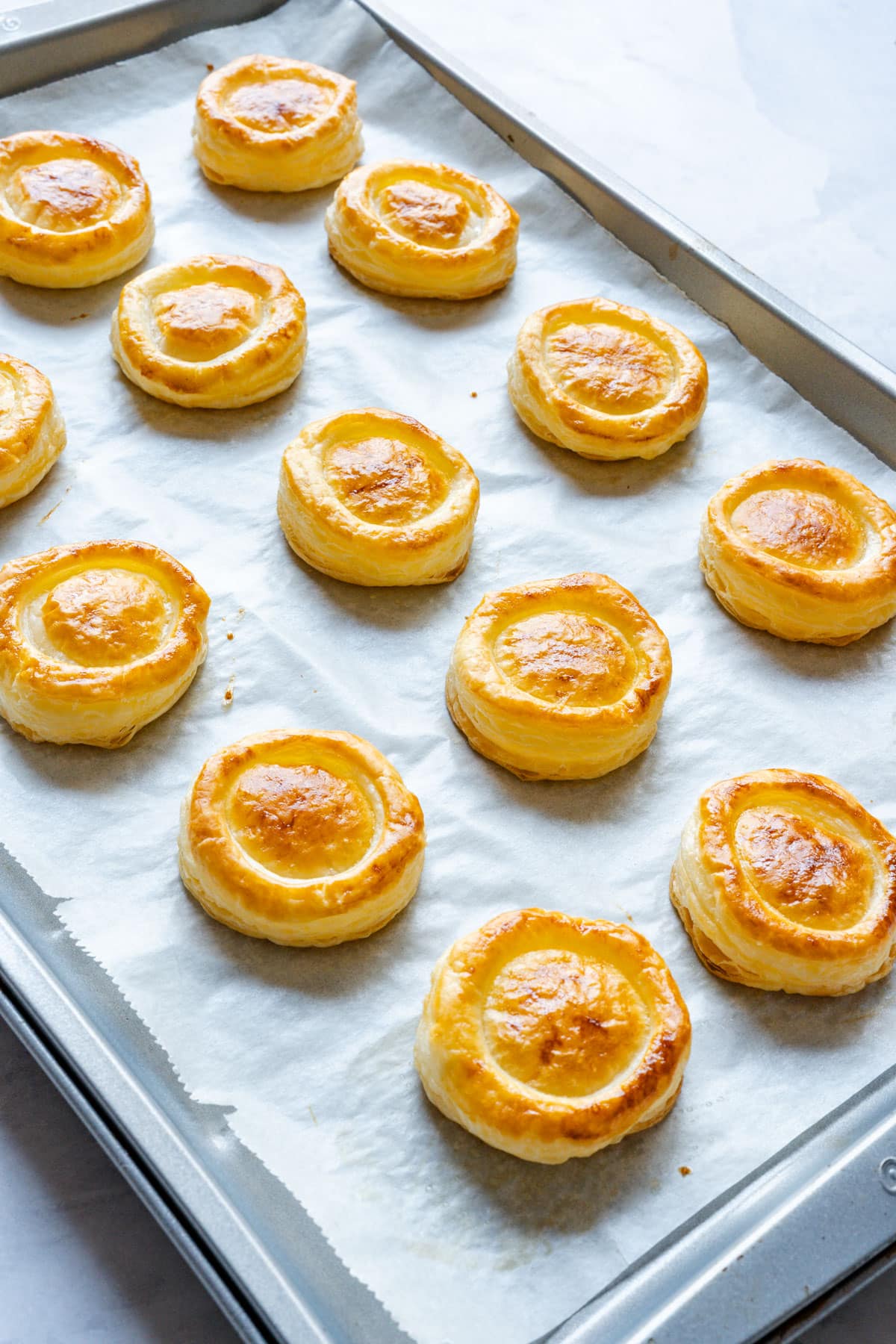 Golden baked pastry cases on a parchment-lined baking sheet, each with a domed center still in place.