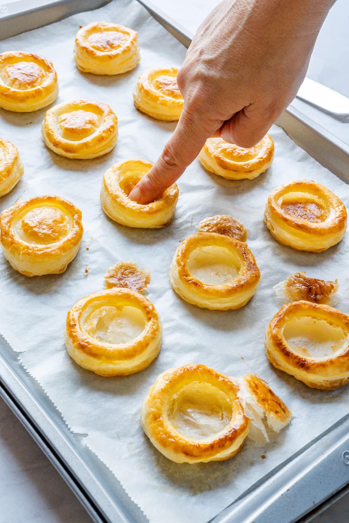 A finger pressing down the risen center of a baked pastry case, with removed caps beside it.