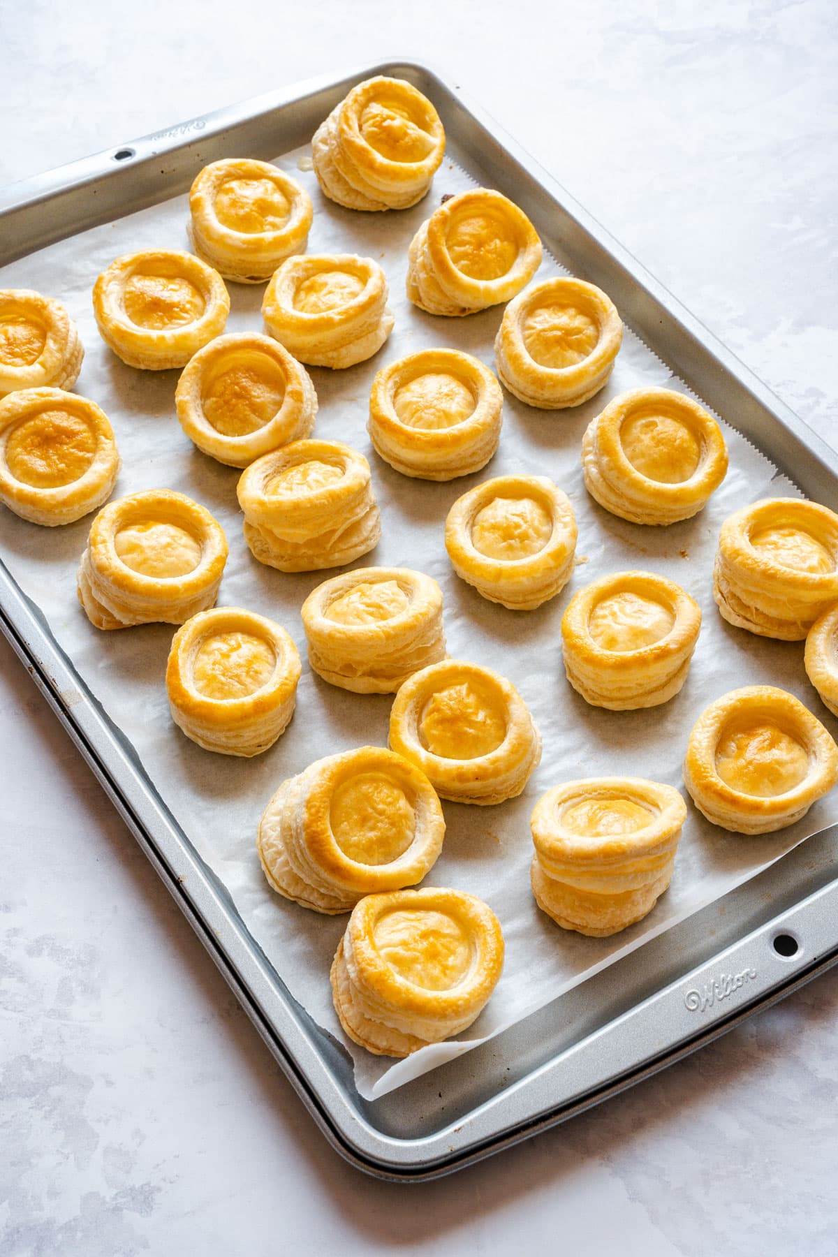 A full tray of baked pastry cases, with some leaning slightly and their raised centers still in place.