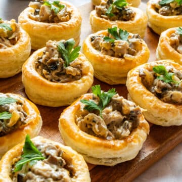 Chicken and mushroom vol-au-vents with a creamy filling, topped with fresh parsley and arranged on a wooden serving board.